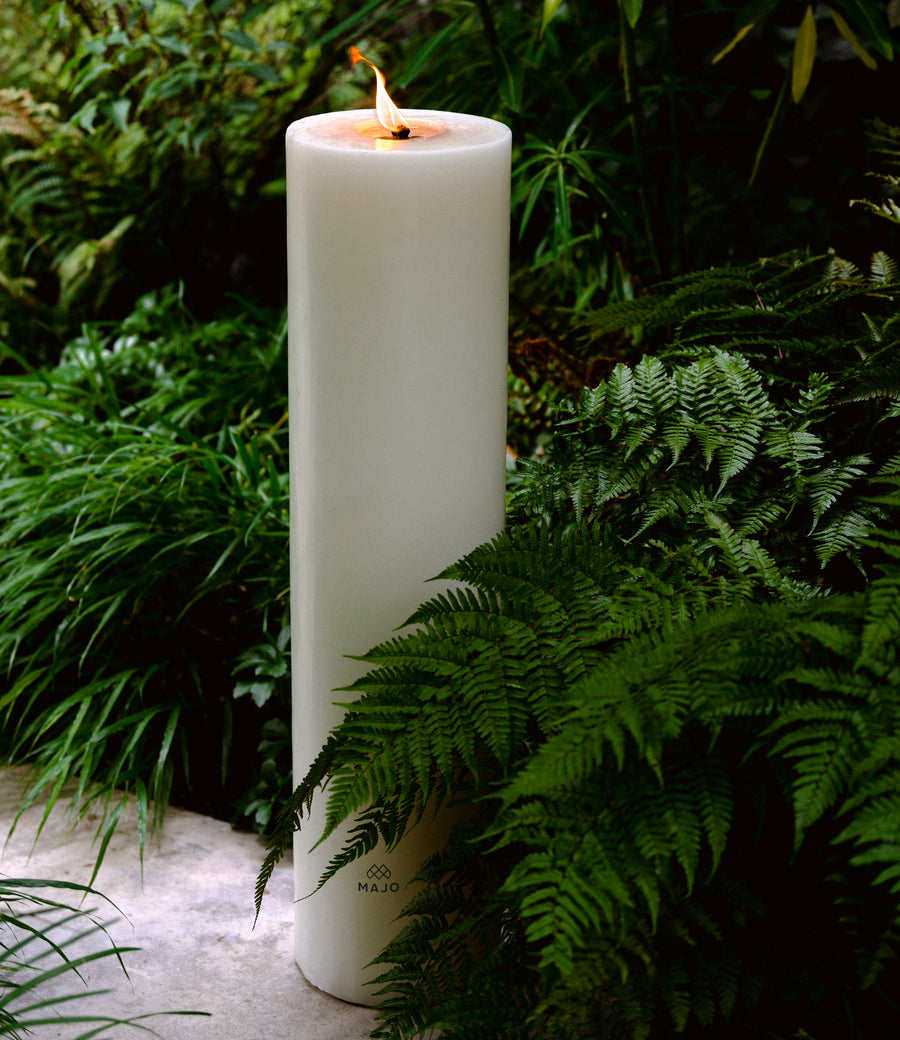 MAJO large outdoor garden candle 80cm tall lit on concrete path with ferns and grass.